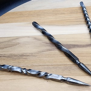 Puede incluir: Tres pinchos de metal retorcidos con puntas puntiagudas, sobre una superficie de madera.