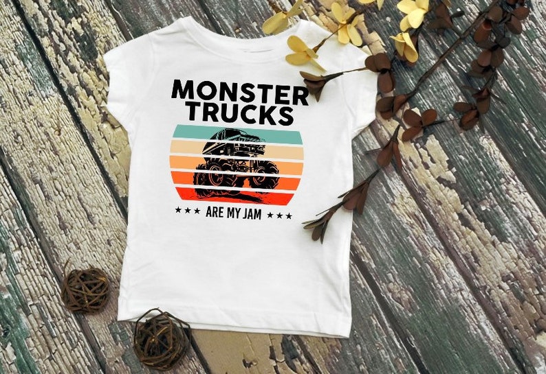 May include: White t-shirt with a black graphic of a monster truck in front of a sunset with the text "Monster Trucks Are My Jam".
