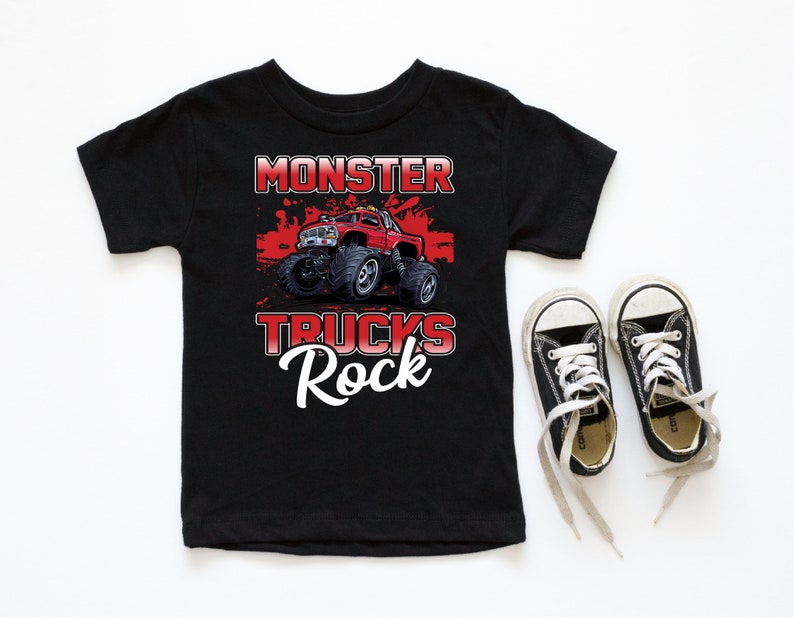 Może przedstawiać: Czarny t-shirt z grafiką czerwonego monster trucka i tekstem "Monster Trucks Rock".