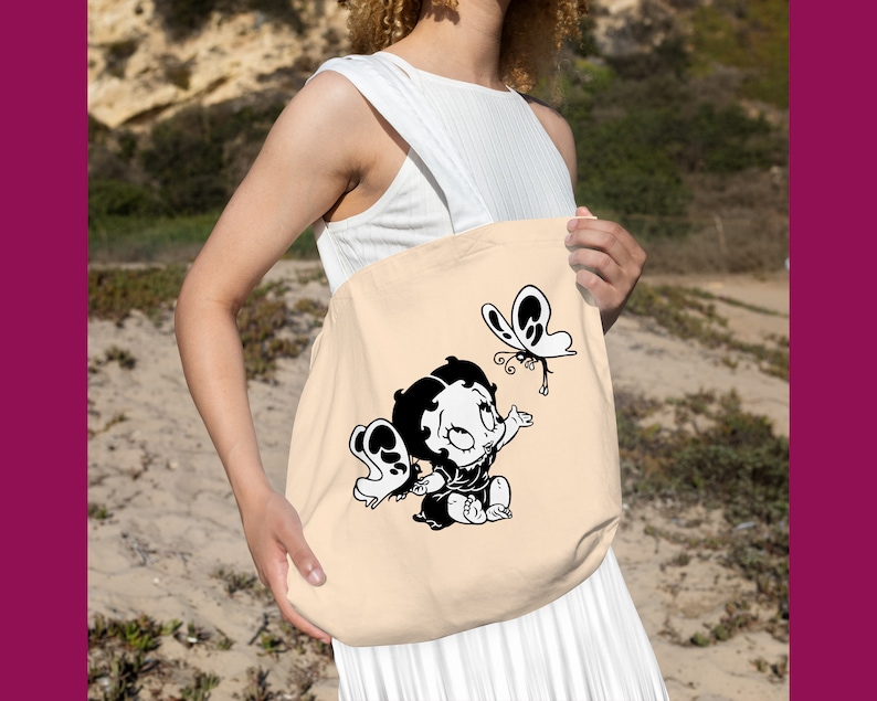 May include: A beige tote bag featuring a black and white cartoon image of a girl with a butterfly. The girl is wearing a dress and has her hair tied back in a ponytail. The butterfly is flying above her head.