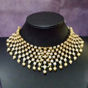May include: A gold choker necklace with a large, intricate design of white stones and a fringe of pearls.