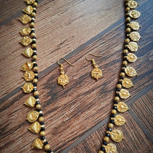 May include: A gold necklace with black beads and gold pendants. The necklace is on a wooden surface. There are also matching earrings.