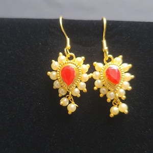 May include: A pair of gold earrings with red gemstone accents and white pearl embellishments.