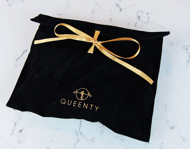 Pu&ograve; includere: Borsa in velluto nero con un nastro dorato legato in un fiocco. La borsa ha il testo "QUEENTY" stampato in oro.