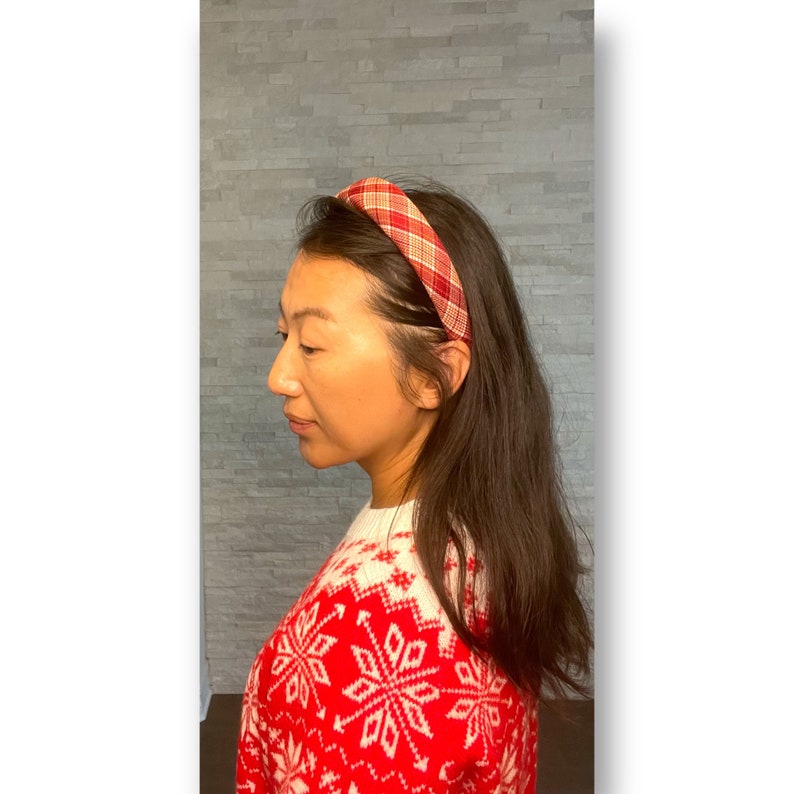 Pu&ograve; includere: Un cerchietto a scacchi rosso e bianco con un design attorcigliato. Il cerchietto &egrave; indossato da una persona con capelli lunghi e castani.