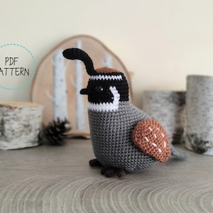 Op de afbeelding: Gehaakte amigurumi kwartel in een bruin, grijs en wit kleurenschema. De kwartel staat op een houten oppervlak met een berkenstam erachter. De tekst "PDF PATTERN" staat in een cirkel aan de linkerkant van de afbeelding.