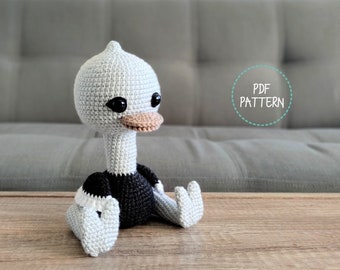 May include: A crocheted amigurumi ostrich toy with a black and white striped shirt. The toy is sitting on a wooden table with a gray couch in the background. The text "PDF PATTERN" is visible in a circle on the couch.