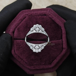May include: A silver-toned ring guard featuring two symmetrical, arched bands adorned with small, clear, round-cut stones. The design includes intricate metalwork with fan-shaped motifs and circular accents, creating an open, decorative frame.