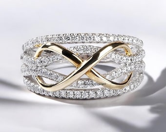 Puede incluir: Un anillo infinito de diamantes y oro. El anillo presenta un diseño de símbolo infinito dorado en el centro, con múltiples bandas de pequeños diamantes brillantes. El anillo está sobre un fondo blanco.