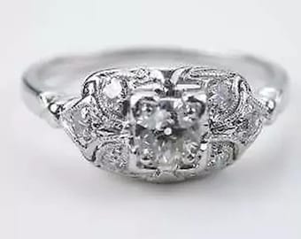 May include: A close-up of a silver ring with a square-cut center stone and smaller accent stones. The ring has an ornate, vintage-inspired design with detailed filigree work. The ring is set against a plain white background.