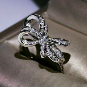May include: A silver ring with a large, sparkling bow design. The bow is made of small, clear stones and is set on a silver band.