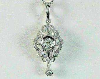 Puede incluir: Un collar con colgante de plata con un diamante redondo central y diamantes más pequeños. El colgante tiene un diseño ornamental y de filigrana con un diamante colgante. La cadena también es de plata.