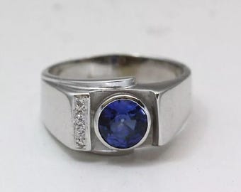 May include: A silver ring with a large, round, deep blue gemstone at the center. The ring has a rectangular band with a small row of clear accent stones on one side.