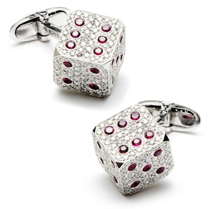 May include: A pair of silver cufflinks in the shape of dice. Each die is encrusted with small, clear stones and features red gemstone dots. The cufflinks have a classic, elegant design.