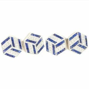 Könnte beinhalten: Ein Paar Manschettenknöpfe mit geometrischem Design. Jeder Manschettenknopf hat eine Würfelform mit abwechselnden Reihen aus blauen und weißen Steinen. Die Manschettenknöpfe sind vor einem weißen Hintergrund platziert.