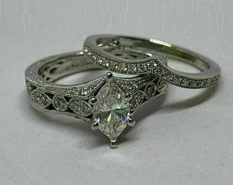 May include: A silver engagement ring set with a marquise-shaped center stone and a matching wedding band. Both rings are adorned with smaller diamonds.