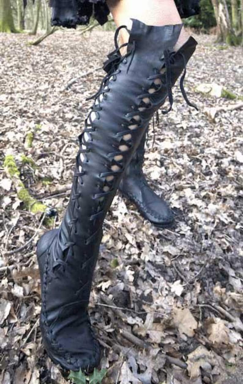 Peut inclure: Une paire de bottes noires montant jusqu'au genou, dot&eacute;es d'un la&ccedil;age frontal sur toute la longueur avec de fins lacets noirs. Les bottes pr&eacute;sentent des coutures visibles sur les bords et une structure souple remontant jusqu'au genou.
