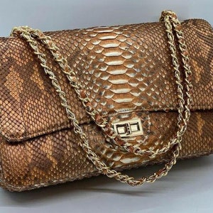 May include: A brown and white snakeskin shoulder bag with a gold chain strap and a gold clasp.