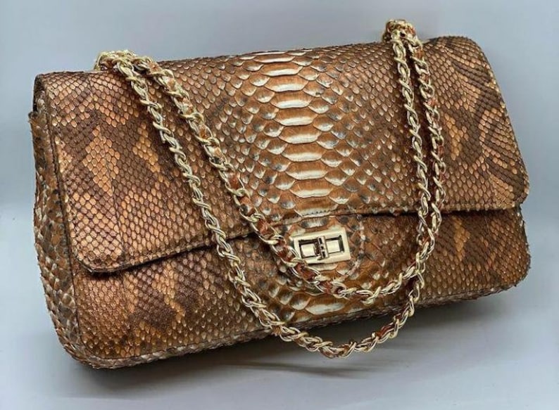 May include: A brown and white snakeskin shoulder bag with a gold chain strap and a gold clasp.