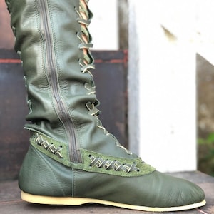 Peut inclure: Une botte vert olive montant jusqu'au genou avec une fermeture &eacute;clair lat&eacute;rale sur toute la longueur, un la&ccedil;age frontal avec des lacets clairs, un empi&egrave;cement en cuir textur&eacute; sur le milieu du pied avec des surpiq&ucirc;res et une semelle plate claire.