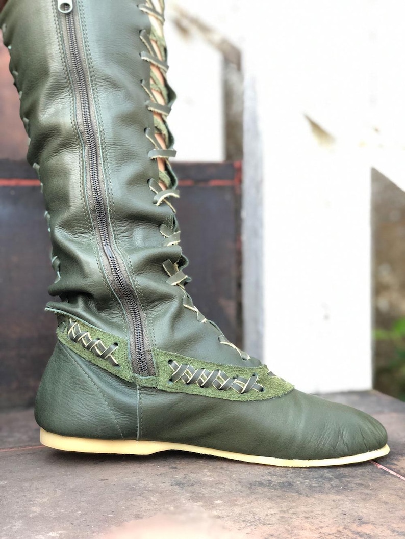 Peut inclure: Une botte vert olive montant jusqu'au genou avec une fermeture &eacute;clair lat&eacute;rale sur toute la longueur, un la&ccedil;age frontal avec des lacets clairs, un empi&egrave;cement en cuir textur&eacute; sur le milieu du pied avec des surpiq&ucirc;res et une semelle plate claire.