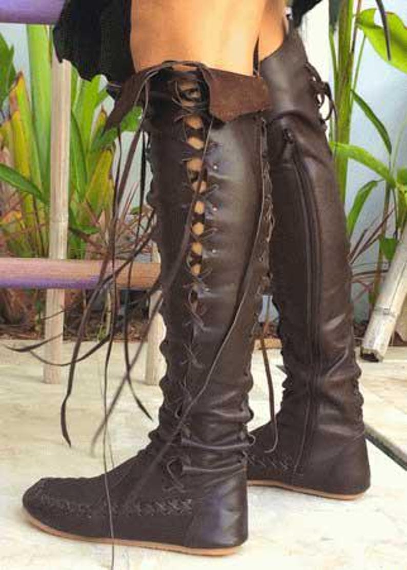 Peut inclure: Une paire de bottes marron fonc&eacute; montant jusqu'au genou, dot&eacute;es d'un la&ccedil;age sur le devant avec de longs liens en cuir, d'un revers en haut et d'une semelle plate. Les bottes pr&eacute;sentent des coutures lat&eacute;rales visibles et une fermeture &eacute;clair.
