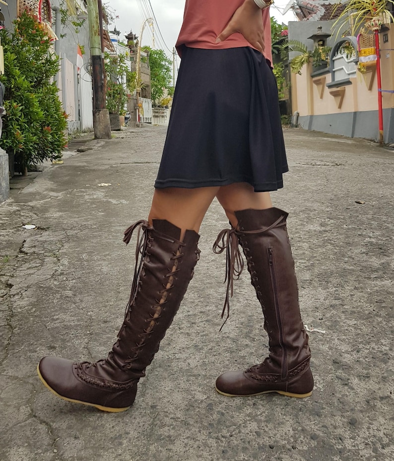Peut inclure: Une paire de bottes marron fonc&eacute; montant jusqu'aux genoux, dot&eacute;es d'un la&ccedil;age sur le devant avec des lacets assortis, d'une fermeture &eacute;clair lat&eacute;rale, d'un bout arrondi et d'une semelle plate. Elles pr&eacute;sentent des d&eacute;tails tress&eacute;s &agrave; la base.