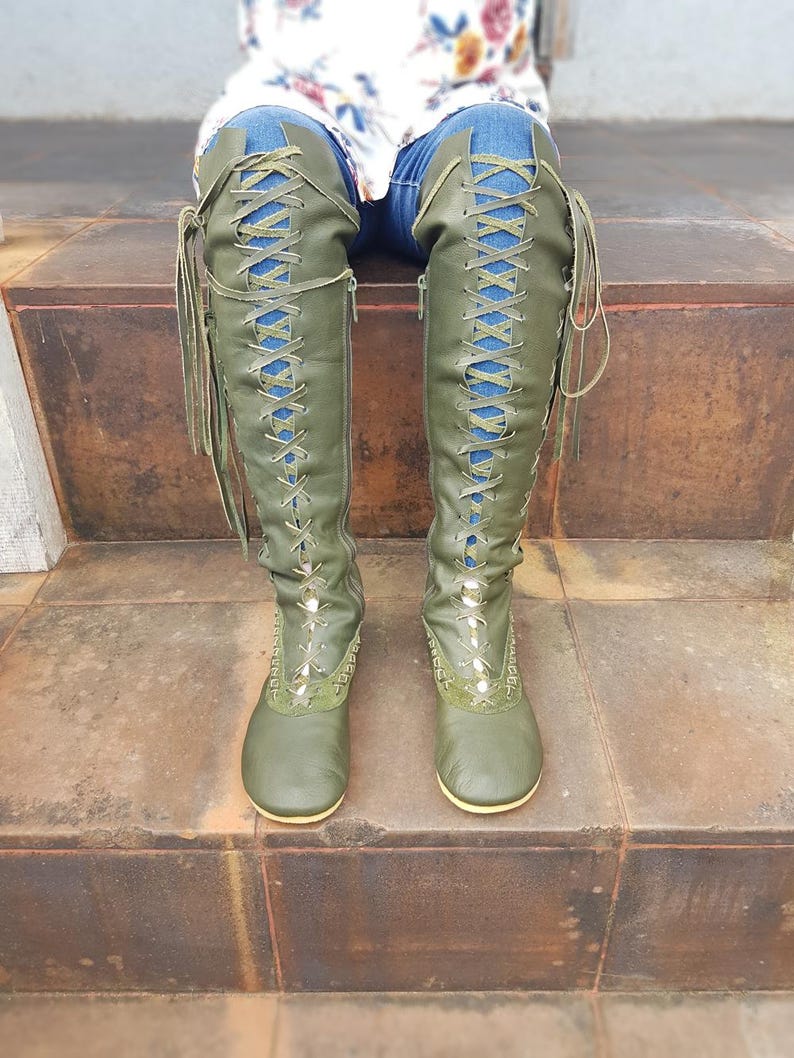 Peut inclure: Bottes vert olive montant jusqu'aux genoux avec un la&ccedil;age frontal sur toute la longueur, des lacets assortis, des fermetures &eacute;clair lat&eacute;rales et des coutures d&eacute;coratives autour des orteils. Les bottes ont une semelle plate et couvrent les jambes.