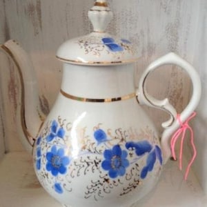 May include: White porcelain teapot with a gold trim and blue floral design. The teapot has a lid with a knob and a handle.