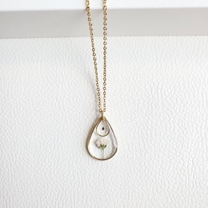 May include: A gold chain necklace with a teardrop-shaped pendant. The pendant is made of clear glass and contains a small white flower.