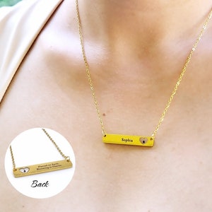 May include: Gold necklace with a bar pendant that says "Sophia" and has a small heart cutout. The back of the pendant says "Planted on Earth, Blooming in Heaven."