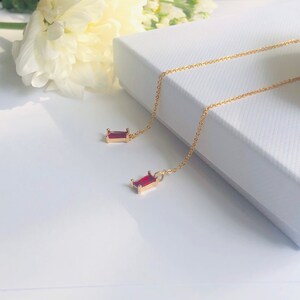May include: A pair of gold chain earrings with red gemstone accents. The earrings are hanging from a white surface.