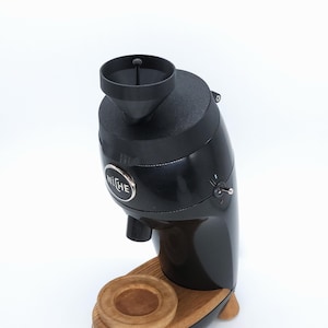 May include: Black coffee grinder with a wooden base and a silver "NICHE" logo. The grinder has a black hopper and a silver chute.