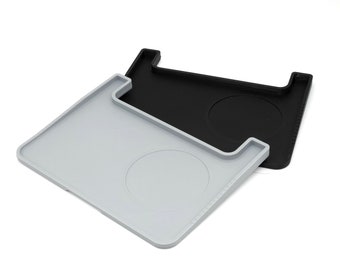 May include: Two silicone trays, one gray and one black, with a circular indentation in the center of each. The trays are designed to hold cups or other small items.