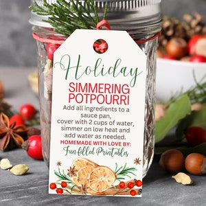 May include: A mason jar filled with potpourri ingredients, adorned with a tag that reads "Holiday Simmering Potpourri." The tag includes instructions and decorative illustrations of oranges, cinnamon sticks, and berries. The jar is tied with a red ribbon and sprigs of greenery.