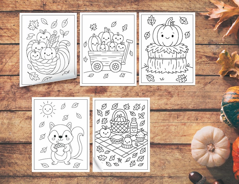 May include: Five black and white coloring pages featuring fall-themed illustrations. The images include pumpkins, a cornucopia, a squirrel with an acorn, and a picnic scene with a smiling cupcake. The pages are on a wooden surface.