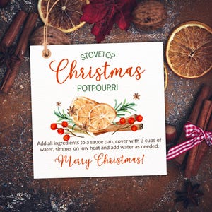 Op de afbeelding: Een wit label met de woorden "Stovetop Christmas Potpourri" in rode letters. Het label bevat een aquarel illustratie van gedroogde sinaasappelschijfjes, kaneelstokjes en bessen. De tekst "Merry Christmas!" is ook opgenomen.