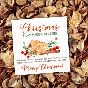 Op de afbeelding: Een vierkante witte kaart met de tekst "Christmas HOMEMADE POTPOURRI" in rood script. De kaart bevat een aquarel illustratie van sinaasappelschijfjes, kaneelstokjes en bessen. De tekst "Merry Christmas!" is ook opgenomen.