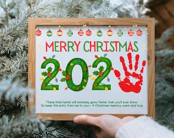 May include: A framed Christmas print with the words "MERRY CHRISTMAS 202" in red and green. The "202" is decorated with holly and lights. A red handprint is on the right. The print includes a sentimental quote about preserving memories.