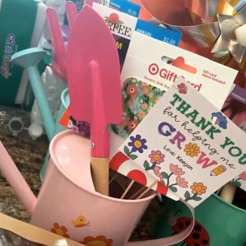 May include: A pink watering can with a flower design, a pink trowel with a wooden handle, and a thank you card with the text "Thank you for helping me grow! Love: Keegan".