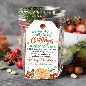 Puede incluir: Un tarro de cristal con tapa plateada y una etiqueta blanca. La etiqueta dice "It's beginning to smell a lot like Christmas" e incluye instrucciones para popurr&iacute; para estufa. El tarro est&aacute; decorado con vegetaci&oacute;n y bayas rojas.
