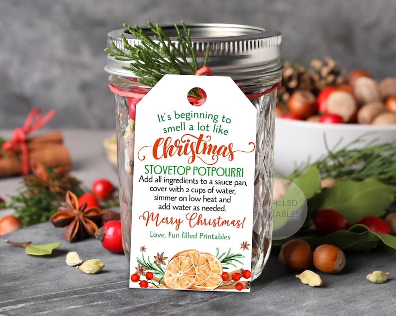 Puede incluir: Un tarro de cristal con tapa plateada y una etiqueta blanca. La etiqueta dice "It's beginning to smell a lot like Christmas" e incluye instrucciones para popurr&iacute; para estufa. El tarro est&aacute; decorado con vegetaci&oacute;n y bayas rojas.