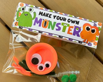Puede incluir: Una bolsa de plástico transparente que contiene materiales para manualidades para hacer un monstruo. La bolsa incluye una tapa naranja, ojos saltones, limpiapipas naranjas y verdes y pompones verdes. La bolsa está etiquetada "MAKE YOUR OWN MONSTER".
