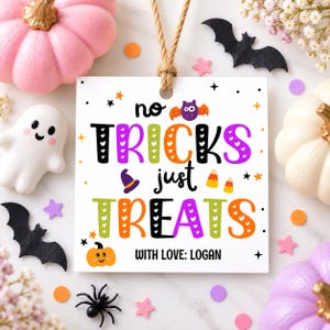 May include: A square white gift tag with a jute twine loop featuring the text "no TRICKS just TREATS" in colorful, patterned letters. The design includes a purple bat, a witch hat, candy corn, a small orange pumpkin, and "WITH LOVE: LOGAN".