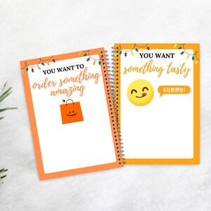 Puede incluir: Dos cuadernos con espiral con bordes naranjas y p&aacute;ginas blancas. Uno tiene el texto "YOU WANT TO order something amazing" y un gr&aacute;fico de bolsa de la compra. El otro dice "YOU WANT something tasty" con una carita sonriente y "YUMMY!"