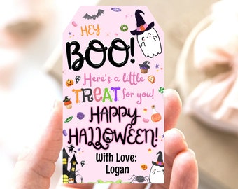 May include: A pink Halloween gift tag with the words "HEY BOO!" and "HAPPY HALLOWEEN!" in black and colorful text. The tag features illustrations of a ghost, a witch's hat, a haunted house, and candy. The tag is personalized with the name "Logan".