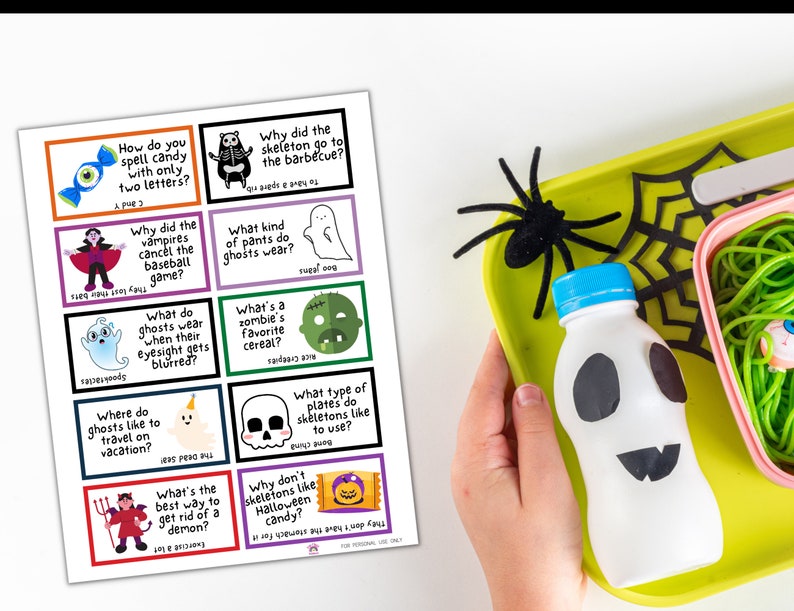 May include: A Halloween-themed lunch tray with a ghost-shaped bottle, spider web, and a sheet of Halloween joke cards. The cards feature colorful illustrations and humorous questions and answers related to Halloween.