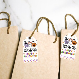 May include: Three brown paper gift bags with rope handles. Each bag has a white tag with Halloween-themed illustrations and text that reads "Here's a treat just for you! Happy Halloween!" The tags feature a ghost, pumpkin, and the word "Boo".