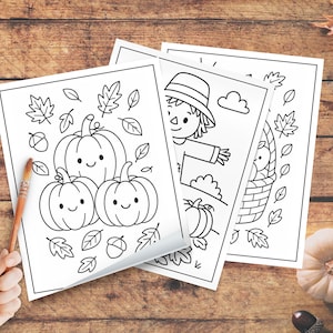 May include: Three black and white coloring pages featuring fall themes. One page shows three smiling pumpkins with leaves and acorns. Another depicts a scarecrow, and the third shows a basket of apples. Paintbrushes are in the lower left corner.