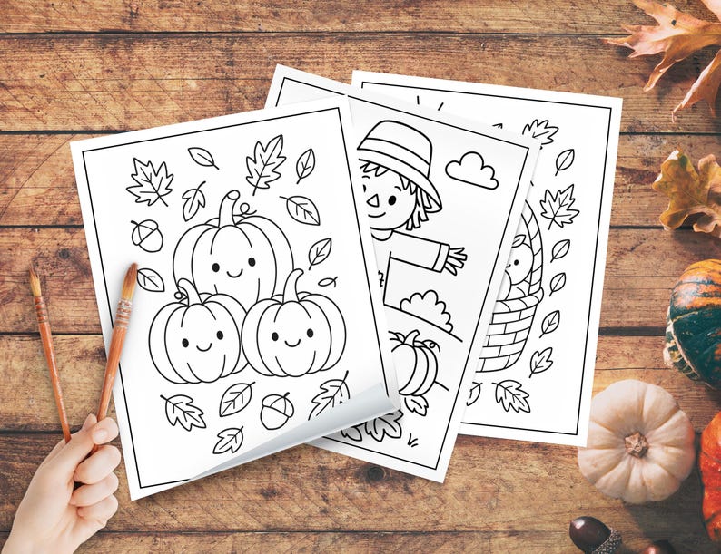 May include: Three black and white coloring pages featuring fall themes. One page shows three smiling pumpkins with leaves and acorns. Another depicts a scarecrow, and the third shows a basket of apples. Paintbrushes are in the lower left corner.